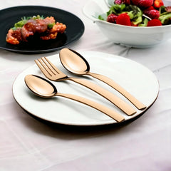 Rose gold cutlery set placed on white plate, with pasta and salad bowls in background.