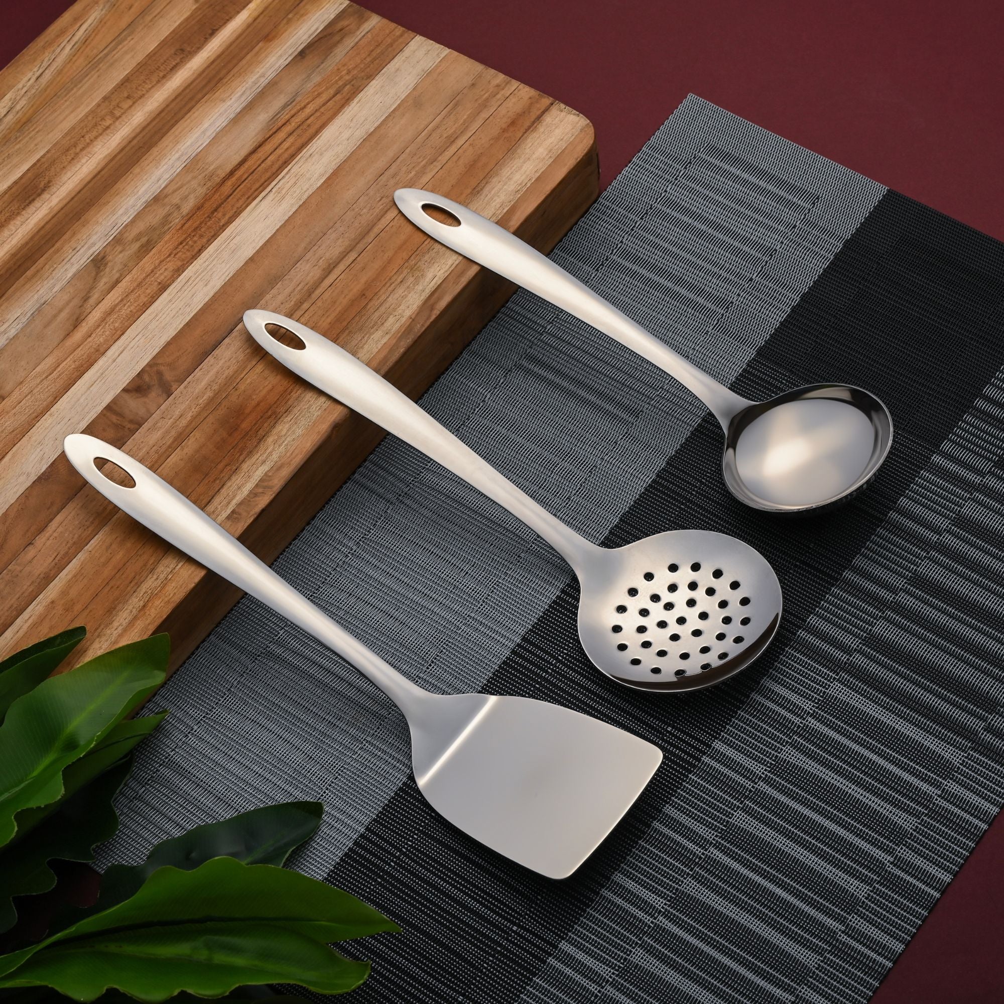 Montavo Amazon serving spoons 3-piece set displayed on gray placemat with wooden cutting board in modern kitchen setting