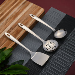 Montavo Amazon serving spoons 3-piece set displayed on gray placemat with wooden cutting board in modern kitchen setting