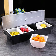 Bar condiment caddy with clear lid opened, displaying four compartments with colorful fruit garnishes including peppers, tomatoes, and lemons with extra bowl beside