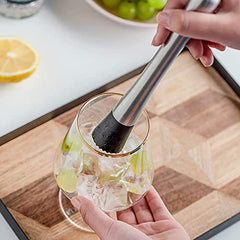Person using stainless steel bar muddler to crush lime in gin and tonic glass on wooden cutting board