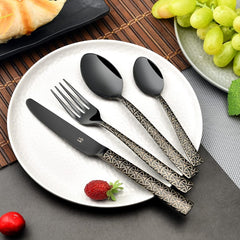 Elegant black cutlery set with geometric handles arranged on white plate, surrounded by fruits and bread.