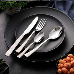 Pebble-design cutlery set neatly arranged on stacked black plates with bowl of snacks beside.