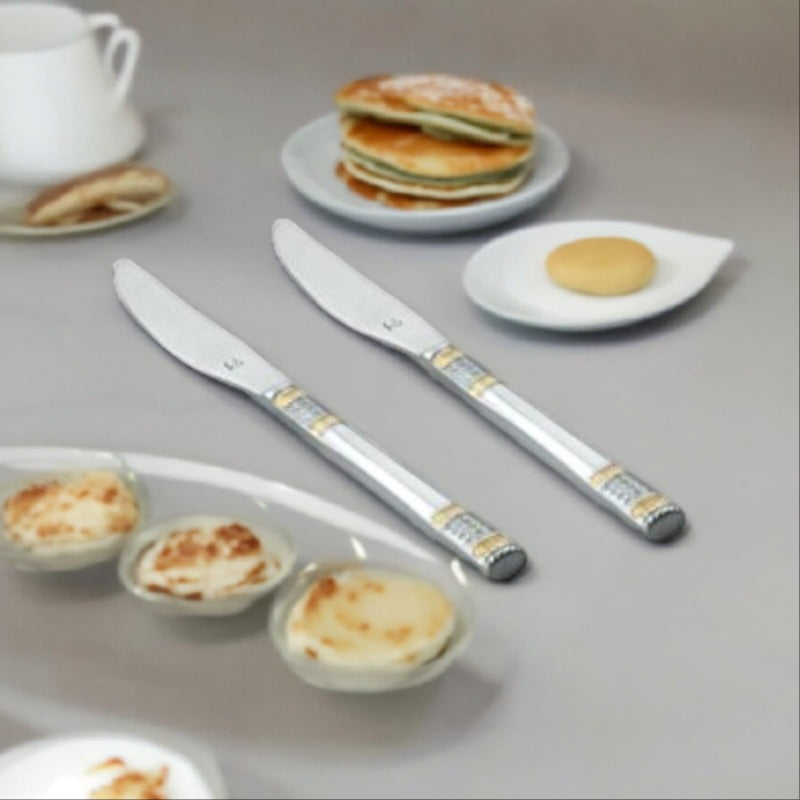 Two stainless steel dinner knives with decorative gold and silver bands on handles, displayed on breakfast table with pancakes and eggs.