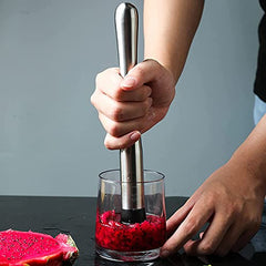 Hands using stainless steel cocktail muddler to crush dragon fruit in clear glass for cocktail preparation