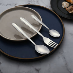 Cutlery set including fork, tablespoon, and teaspoon arranged diagonally across stacked plates on marble background.