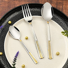 Stylish silver and gold flatware set placed elegantly on ceramic plate over a rustic wooden table.