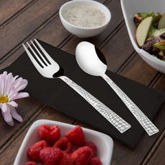 Modern fork and spoon with geometric handles placed on black plate, surrounded by assorted fresh food.