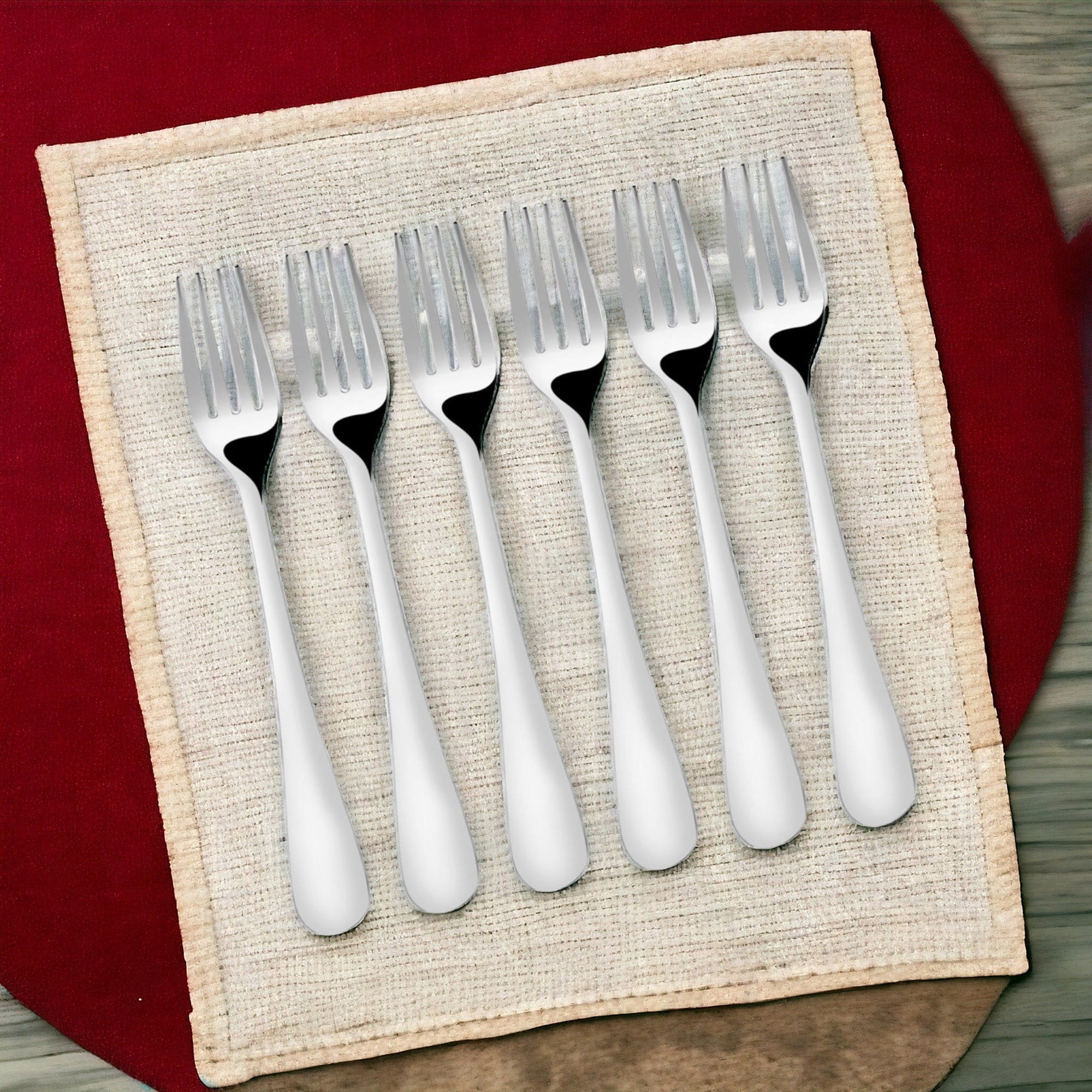 Six dinner forks displayed on woven placemat with red background