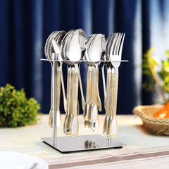 Gold-accented stainless cutlery displayed in upright stand on dining table with elegant curtain background.