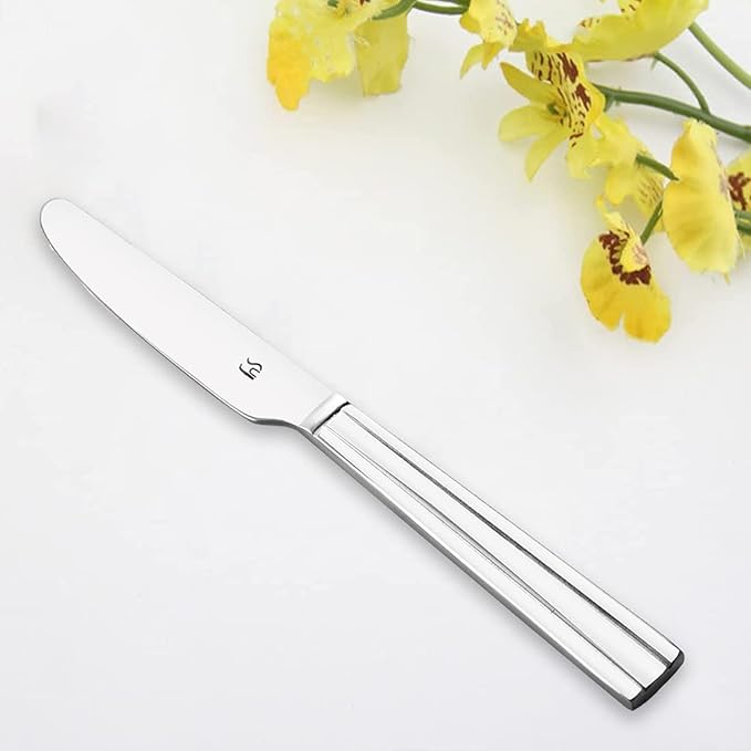 Elegant stainless steel dinner knife with mirror finish and tapered handle displayed on white marble surface beside fresh yellow orchid flowers.