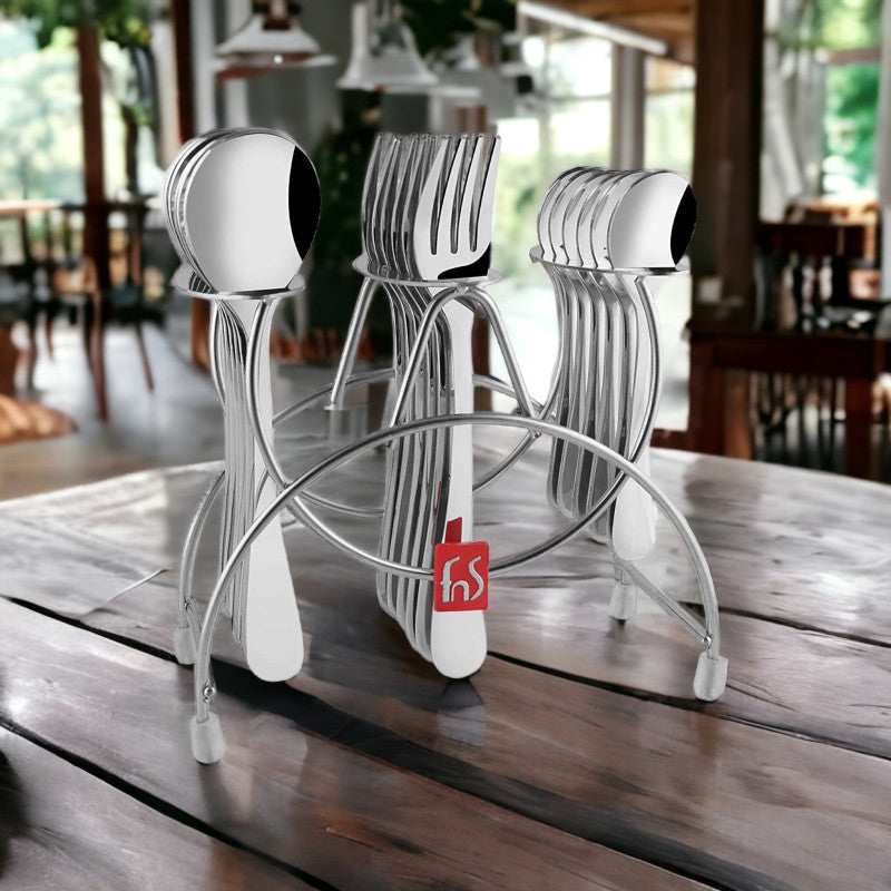 Stainless steel cutlery stand with utensils placed on a rustic wooden table in a cozy cafe setting.
