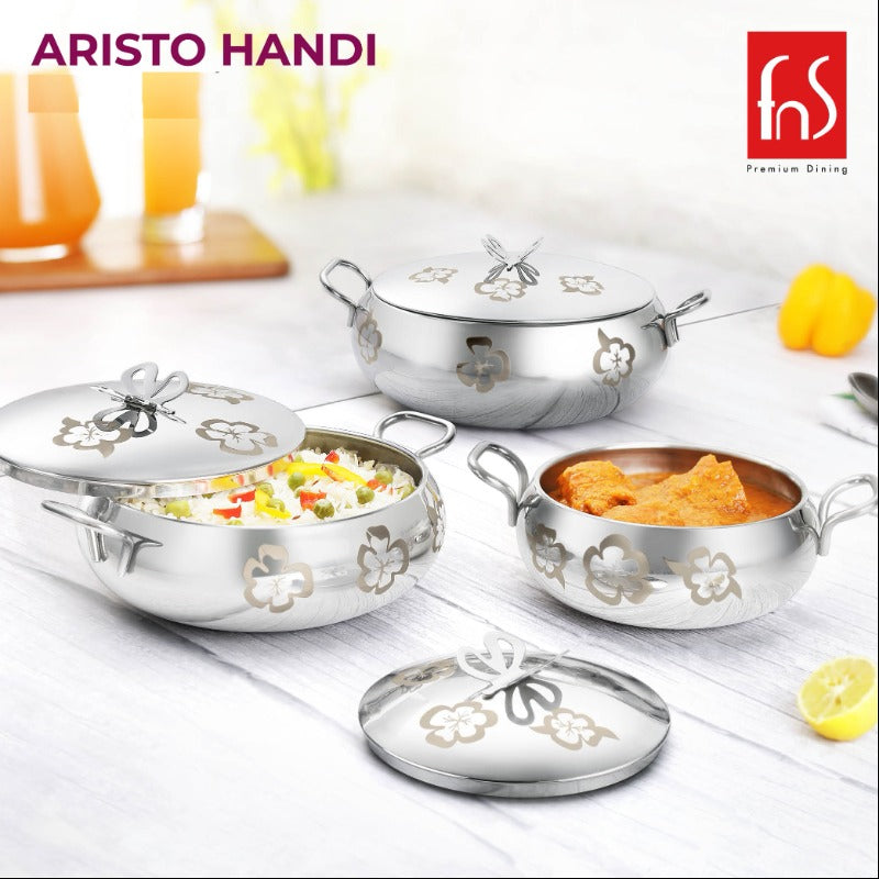 FNS Aristo Handi stainless steel floral butterfly design serving handi set with lids, styled with rice and curry on a kitchen surface with juice glasses