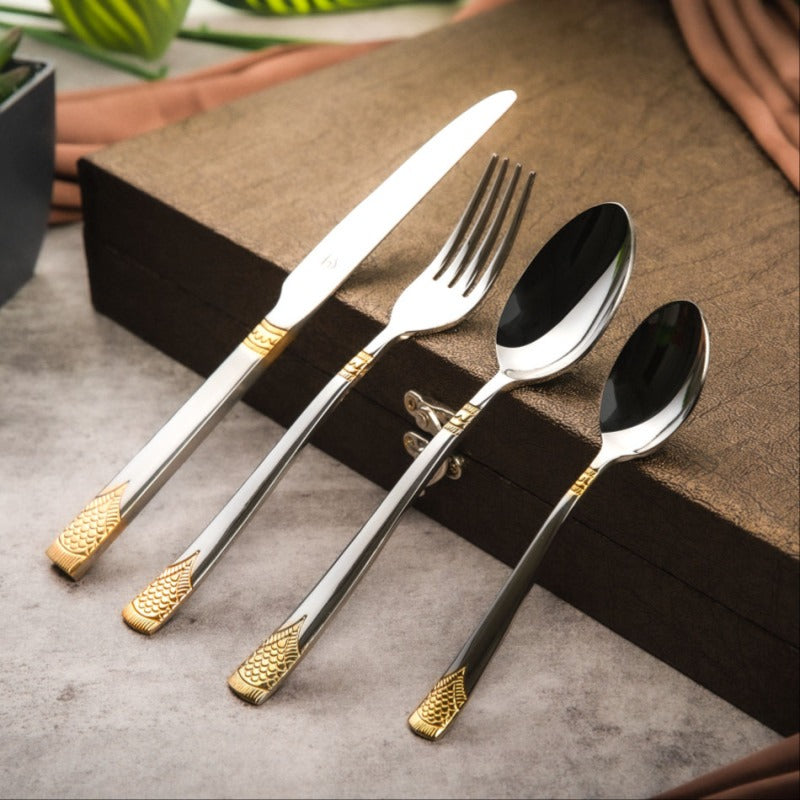 Gold-accented stainless steel knife, fork, and spoons placed neatly on a textured brown box.