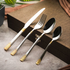 Gold-accented stainless steel knife, fork, and spoons placed neatly on a textured brown box.