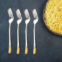 Four August Dinner Forks are placed upright beside a bowl of cooked yellow noodles on a textured dark surface, highlighting the gold-plated handles.