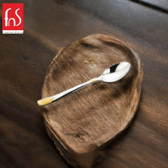 Single stainless steel teaspoon with gold-textured handle tip placed diagonally on rustic wooden heart-shaped dish, FnS Premium Dining logo in corner