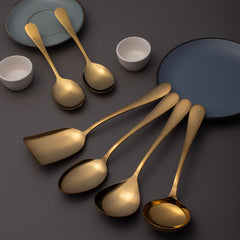 FNS Aurik gold plated 6-piece serving utensil set lifestyle display on dark gray surface with blue and white ceramic plates and bowls