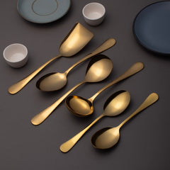 FNS Aurik gold plated stainless steel 6-piece serving set arranged diagonally on dark gray surface with modern ceramic dinnerware and white bowls