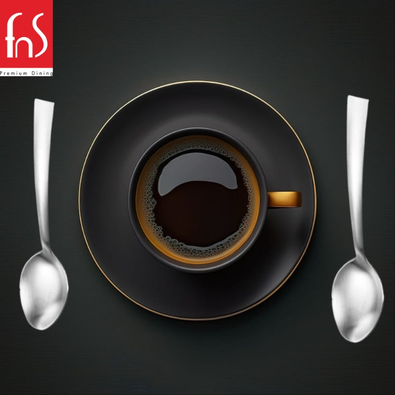 FNS Premium Dining Casper coffee spoons with satin matte finish displayed beside black espresso cup with gold rim on matching saucer against dark textured background