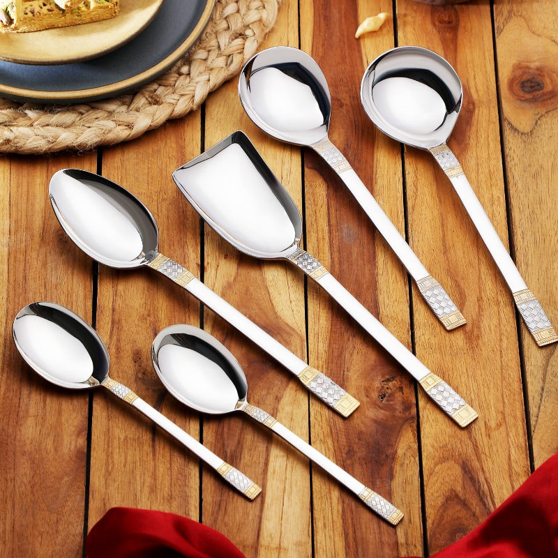 FNS Celebration 6-piece gold-plated serving spoon set displayed on wooden table with plates and woven placemat, showcasing textured gold accent handle design.