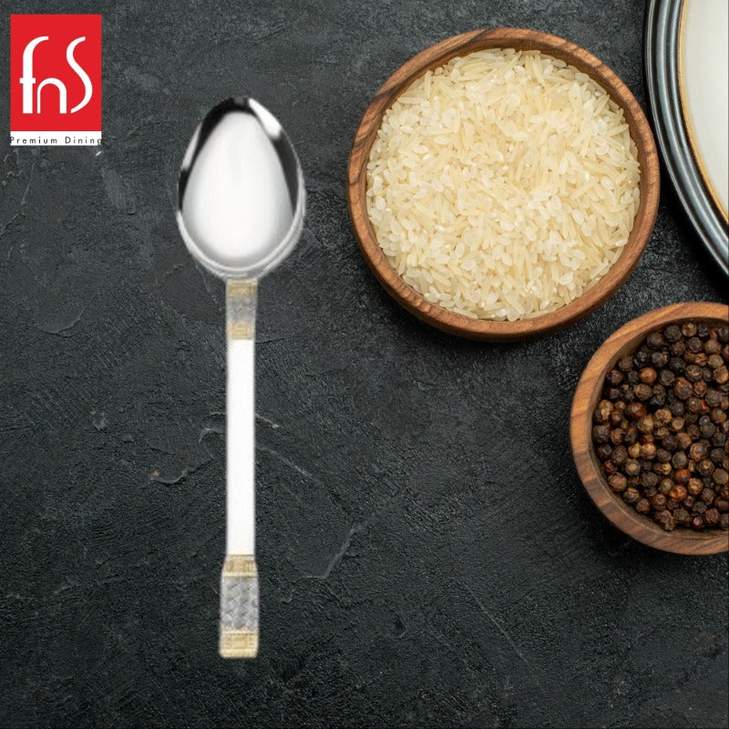 FNS Celebration 24 karat gold plated veg serving spoon displayed on dark slate with wooden bowls of rice and black peppercorns.