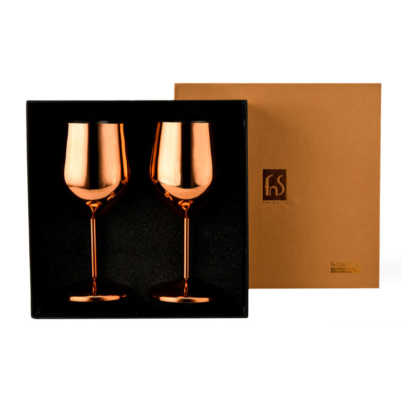 Two rose gold-finish stainless steel wine goblets nestled side by side in a black foam-lined display box, with the matching gold FNS Premium Dining gift box lid leaning open beside it, labeled 'Goblets' on the front.