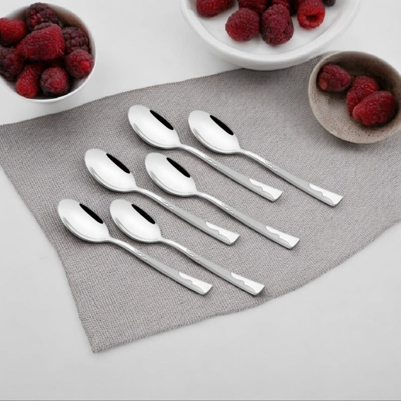 Six Creta stainless steel baby spoons with engraved handles arranged diagonally on a white background.