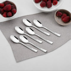 Six Creta stainless steel baby spoons with engraved handles arranged diagonally on a white background.