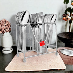Elegant stainless steel cutlery set in stand placed on kitchen counter beside vase and decorative items.