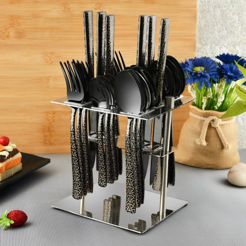Stylish black cutlery set with geometric handles displayed in mirror stand beside flowers and desserts.
