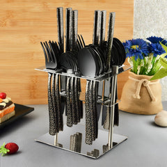 Stylish black cutlery set with geometric handles displayed in mirror stand beside flowers and desserts.