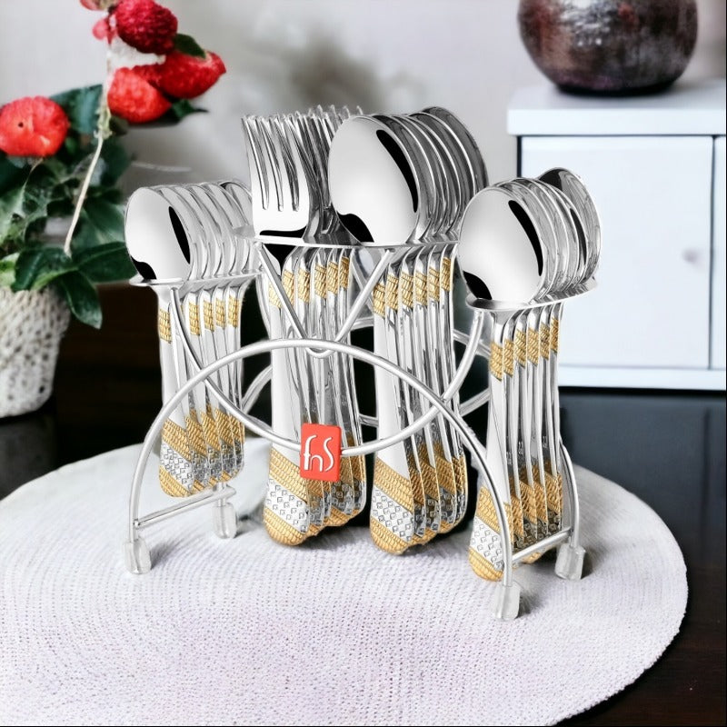 Complete silver cutlery set with gold-accented handles in stand, placed on a round white mat.