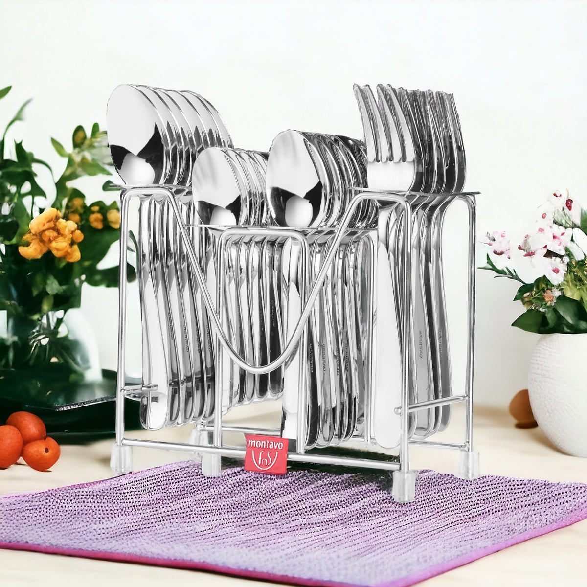 Stainless steel Montavo cutlery set in a rack on table with flowers and fruits in background.