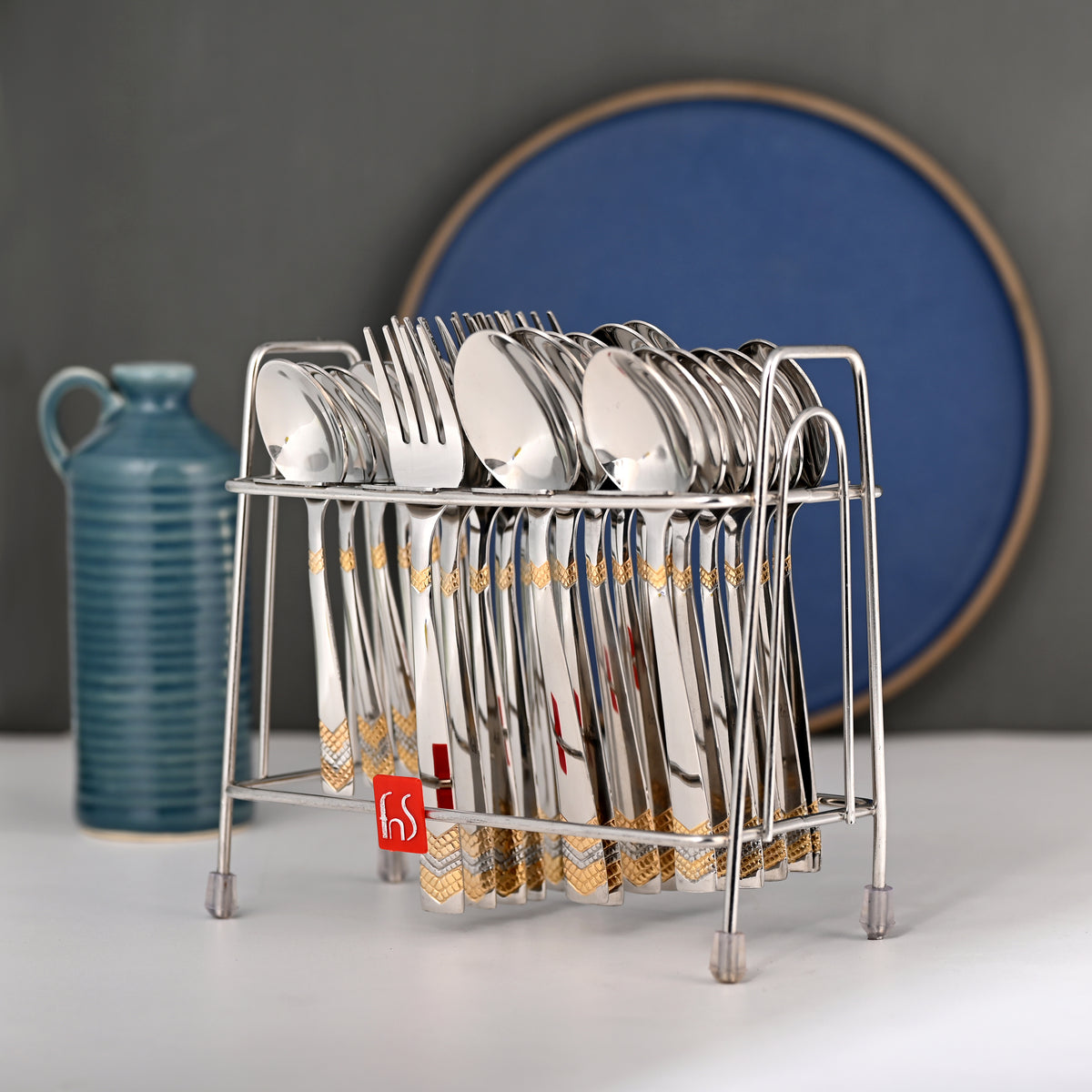 Full cutlery set in silver stand placed on table with decorative jug and blue circular backdrop.