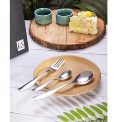 Modern stainless steel cutlery set on ceramic plate, styled with dessert, cups, and wooden serving board.