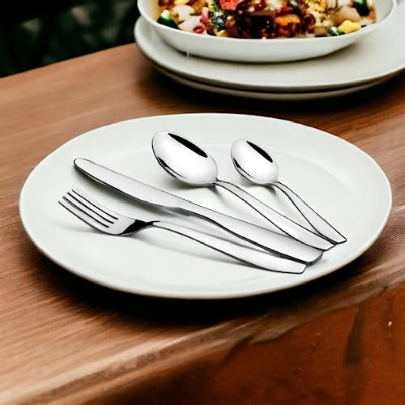 Polished silver cutlery set placed neatly on a white plate beside a dish of colorful food.