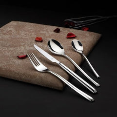 Elegant stainless steel cutlery set displayed on textured napkin with scattered rose petals and dark background.