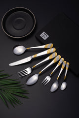 Stylish gold-detailed cutlery set with black plate and branded box placed on matte black background.
