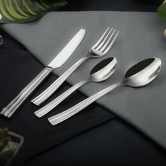 Polished four-piece cutlery set arranged neatly on grey napkin with subtle leaf and plant accents.