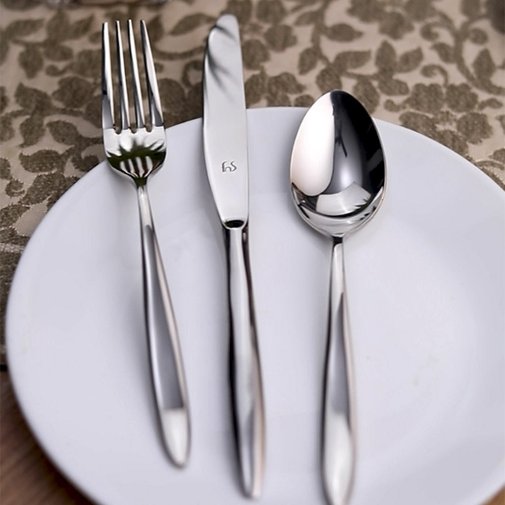 Stainless steel fork, knife, and spoon neatly arranged on a white plate over floral placemat.