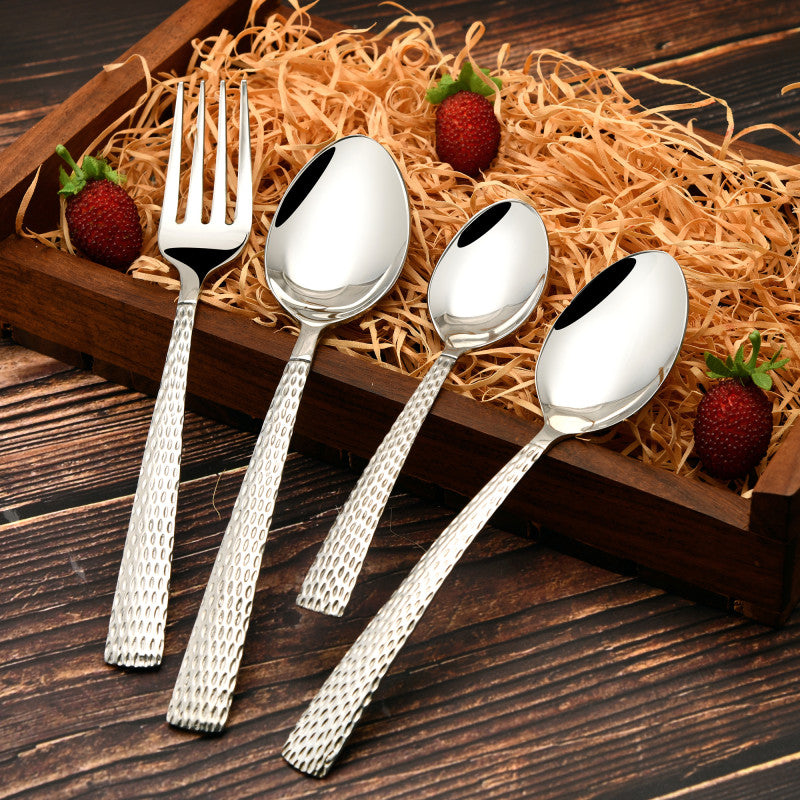 Decorative tray with fork and spoons featuring textured handles, surrounded by hay and fresh strawberries.