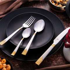 Polished gold-accented cutlery set displayed neatly on matte black dinner plates with snacks nearby.