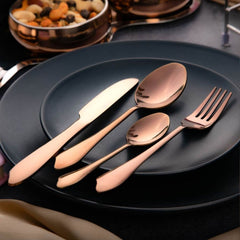 Rose gold cutlery placed on stacked black plates, surrounded by copper snack bowls on dark table.