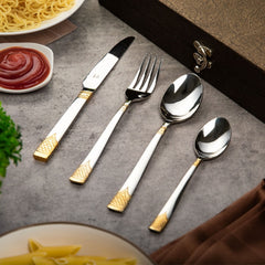 Knife, fork, spoon, and teaspoon with gold accents placed near food and a textured brown box.