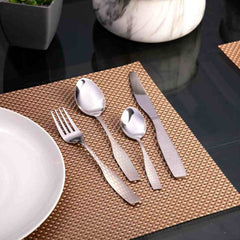 Textured silver cutlery set neatly arranged on woven brown placemat next to a white ceramic plate.