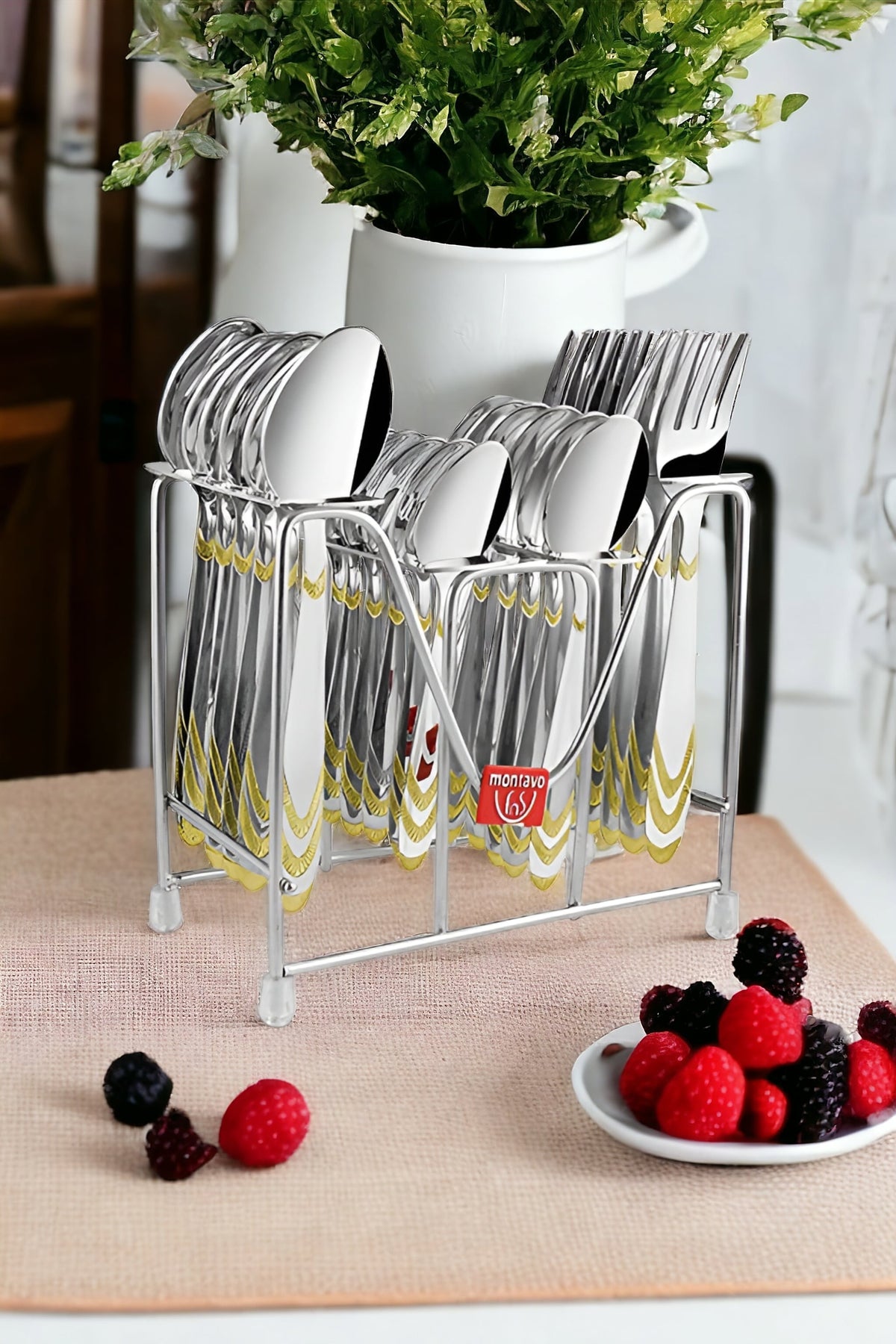 Polished cutlery set in metal stand placed on table beside berries and white ceramic vase.