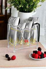 Polished cutlery set in metal stand placed on table beside berries and white ceramic vase.