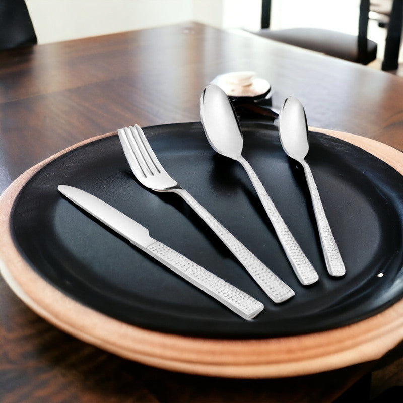 Four-piece cutlery set displayed on black dinner plate with natural wooden edge, modern setting.