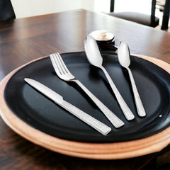 Four-piece cutlery set displayed on black dinner plate with natural wooden edge, modern setting.
